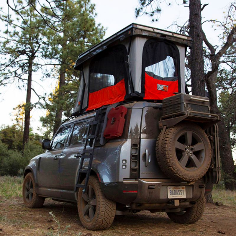 Badass Tents "CONVOY" 2020-23 Land Rover NEW Defender 110 Rooftop Tent PRE-ASSEMBLED. Rear corner view of open tent on vehicle at campsite