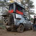 Badass Tents "CONVOY" 2020-23 Land Rover NEW Defender 110 Rooftop Tent PRE-ASSEMBLED. Rear view of open tent on vehicle at campsite with person