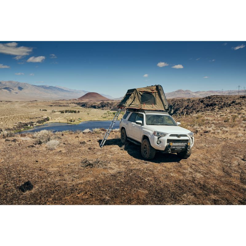 Tuff Stuff Overland Alpha II Hard Shell Rooftop Side Open Tent (2 Person).Front view of open tent on vehicle with ladder in field