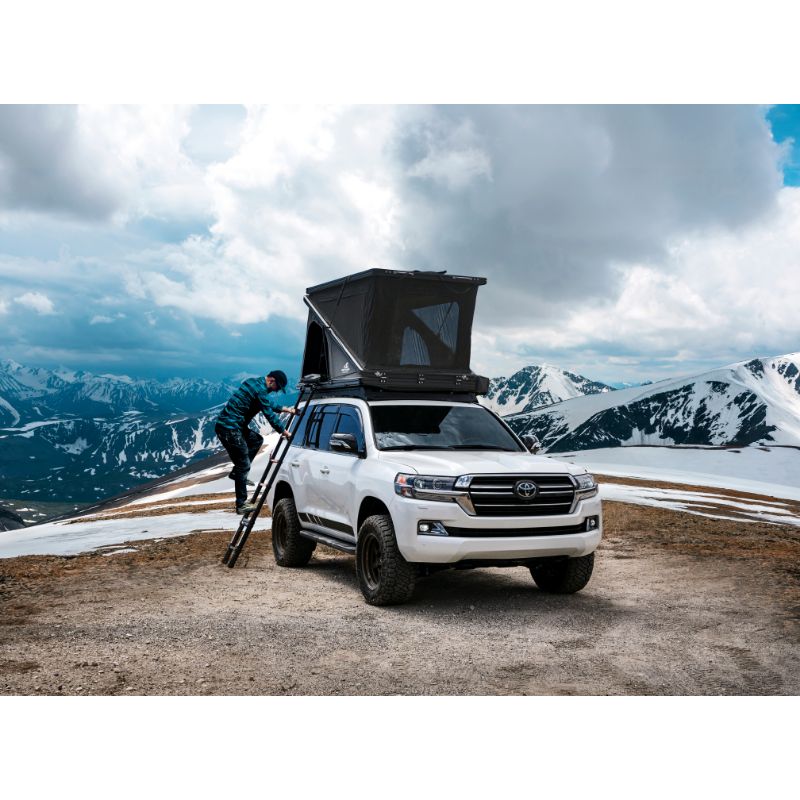 Tuff Stuff Overland Alpine 51 Hard Shell (Aluminum) Roof Top Tent. Front view on person climbing ladder into open tent on vehicle