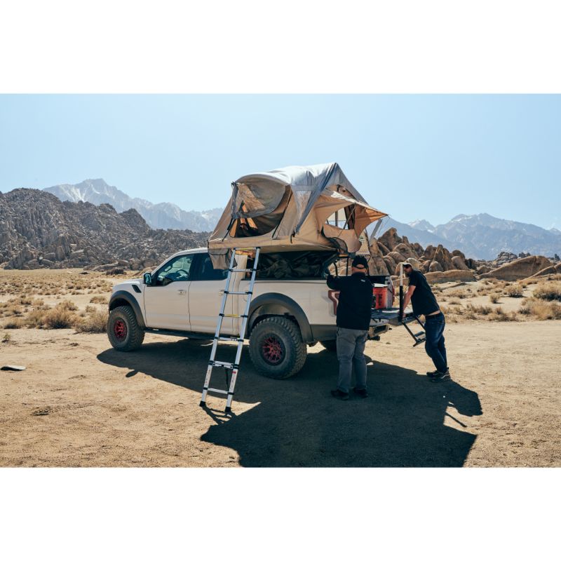 Tuff Stuff Overland Trailhead Soft Shell Rooftop Tent (2 Person). Rear view of open tent on vehicle with ladder and people