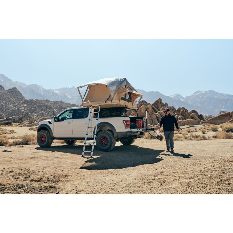 Tuff Stuff Overland Trailhead Soft Shell Rooftop Tent (2 Person). Rear view of open tent on vehicle with ladder and people